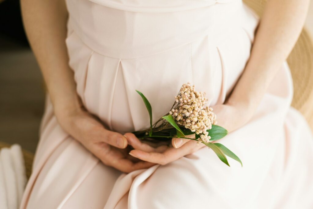 A pregnant woman holds a small bouquet of flowers in her hands. A young woman in a delicate pink mat